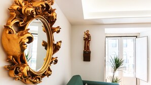 Une pièce comprenant un grand miroir doré à motifs, un canapé vert et une statue murale.
