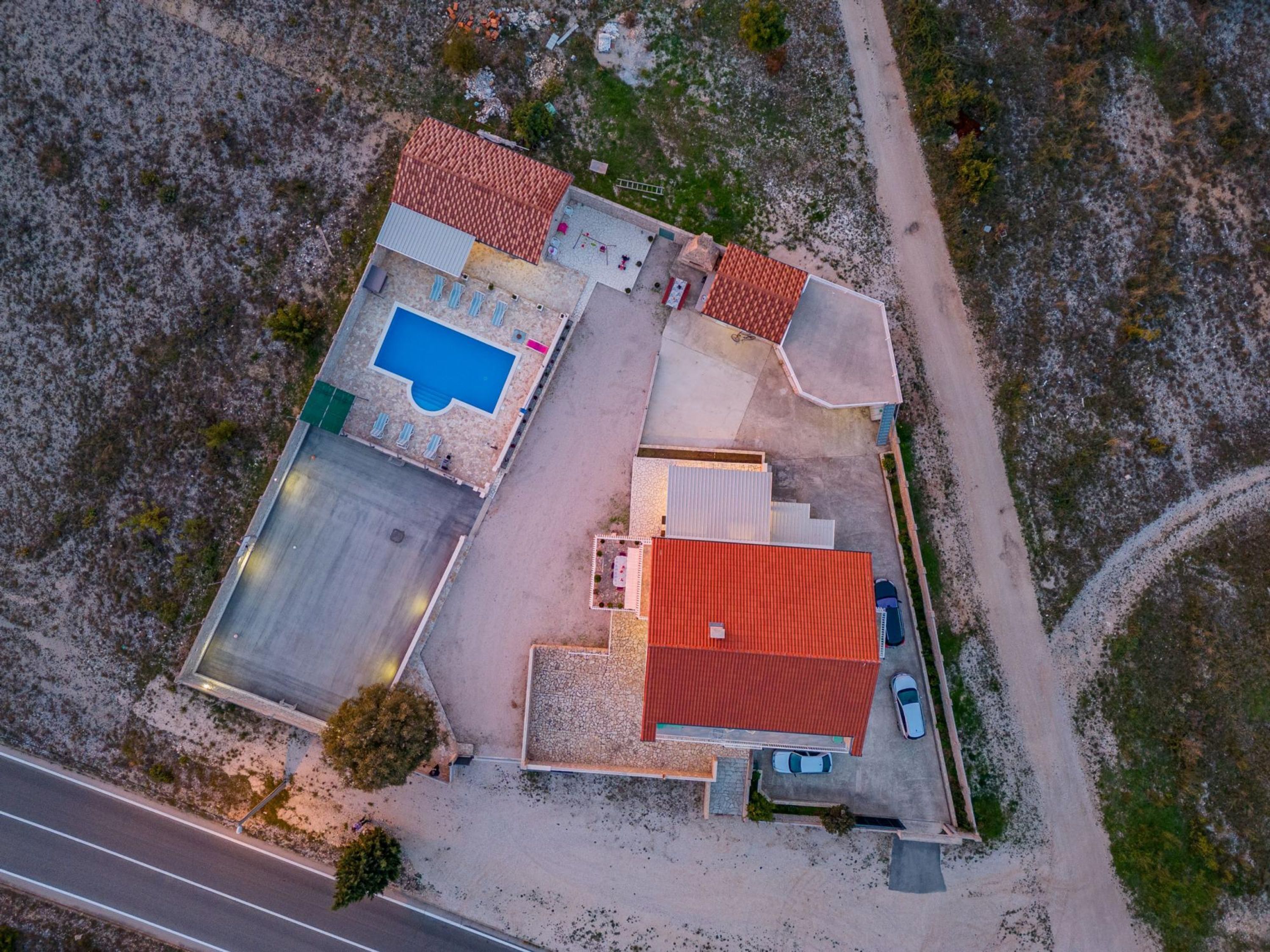Vista aérea de una propiedad con piscina, zona de estacionamiento y un edificio de techo rojo.