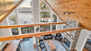 Un vaste espace de vie aménagé dans un style industriel, avec une cheminée en pierre, des poutres en bois et de grandes fenêtres donnant sur un lac.