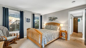 Een slaapkamer met een bed, een stoel, een nachtkastje en een raam met gordijnen.