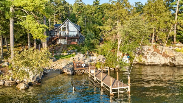 Un chalet au bord du lac, doté d’un quai s’avançant dans l’eau, et entouré d’une forêt dense.