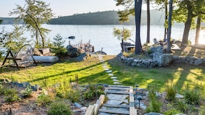 Une terrasse au bord du lac, avec un chemin de pierres menant à un quai, le tout entouré de rochers et de verdure.