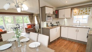 A modern kitchen with white cabinets, a microwave, and a sink. There is a dining area with a table set for four. - Bock Retreat (Morpeth)