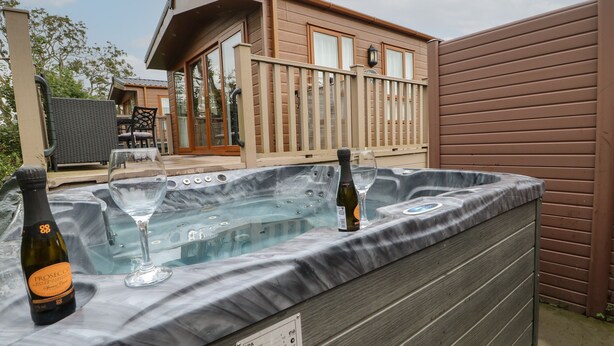 A hot tub with two bottles of wine and glasses, a wooden deck, and a building in the background. - Bock Retreat (Morpeth)