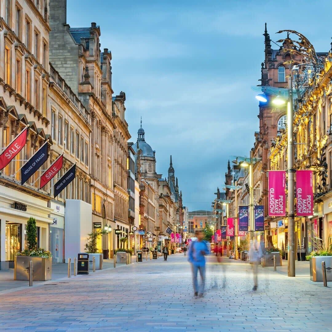 A cobblestone street lined with historic buildings, some with 'SALE' banners, and a few with 'HOUSE OF FRASER' signs.