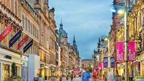 Una calle adoquinada bordeada por edificios históricos, algunos con pancartas de 'SALE' y algunos con letreros de 'HOUSE OF FRASER'.