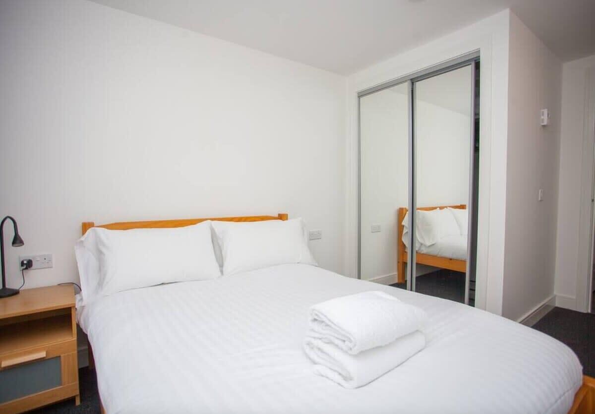 Habitación de hotel con cama, mesita de noche, lámpara y armario con puerta corredera.