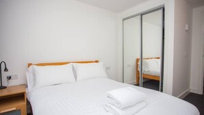 Habitación de hotel con cama, mesita de noche, lámpara y armario con puerta corredera.