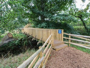 Un pont en bois sur lequel est affiché un panneau d’avertissement indiquant que la surface est glissante par temps humide.