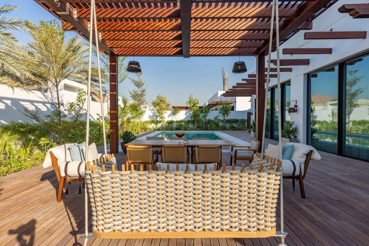 A wooden deck with a pool table, lounge chairs, and a swing chair.