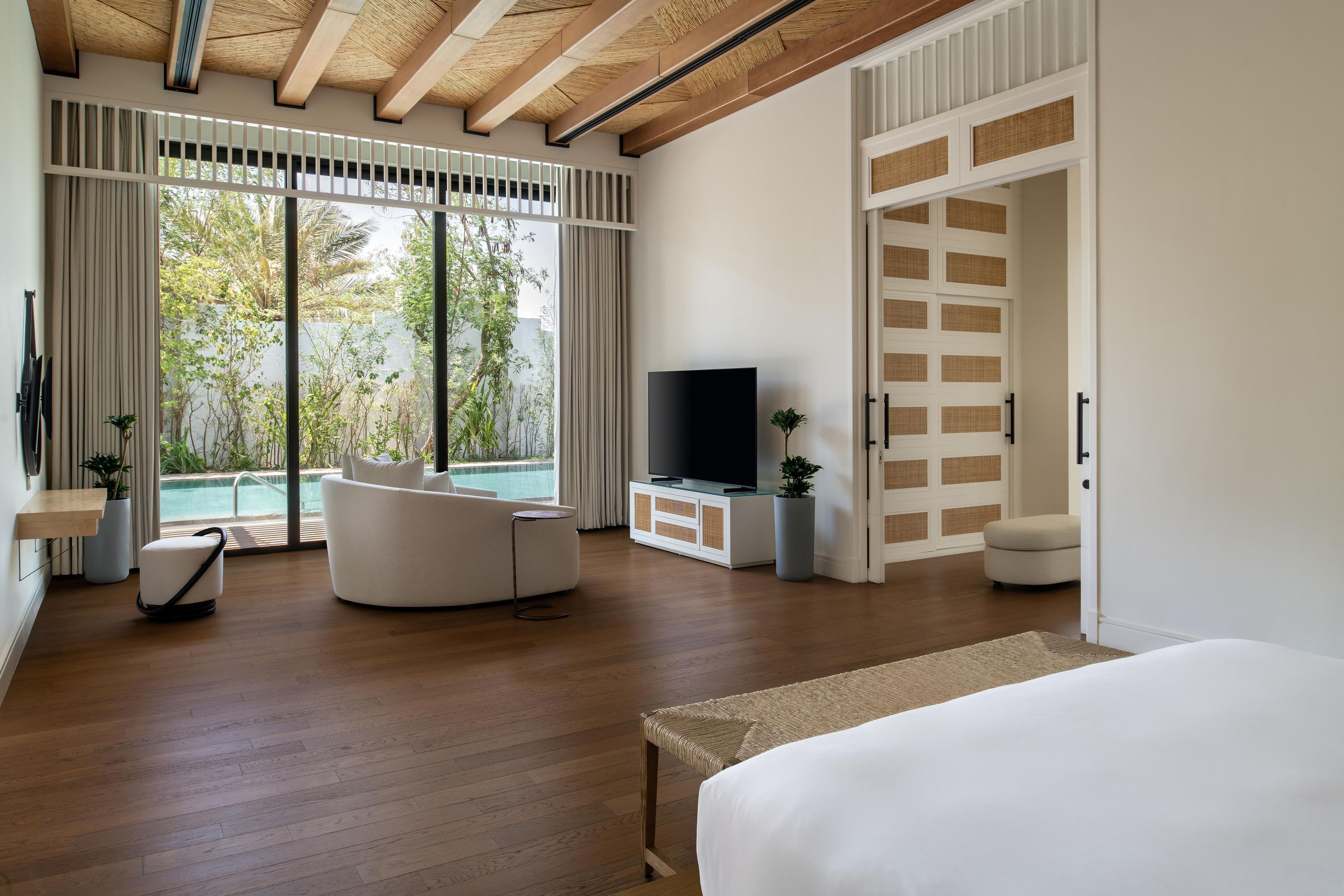 Un dormitorio moderno con una cama grande, televisor, sofá y vistas a una piscina.