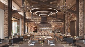 Een ruim restaurant met hoge plafonds, zichtbare balken en diverse verlichtingsarmaturen. Tafels zijn klaar voor dineren, en het interieur heeft stenen muren en houten balken.
