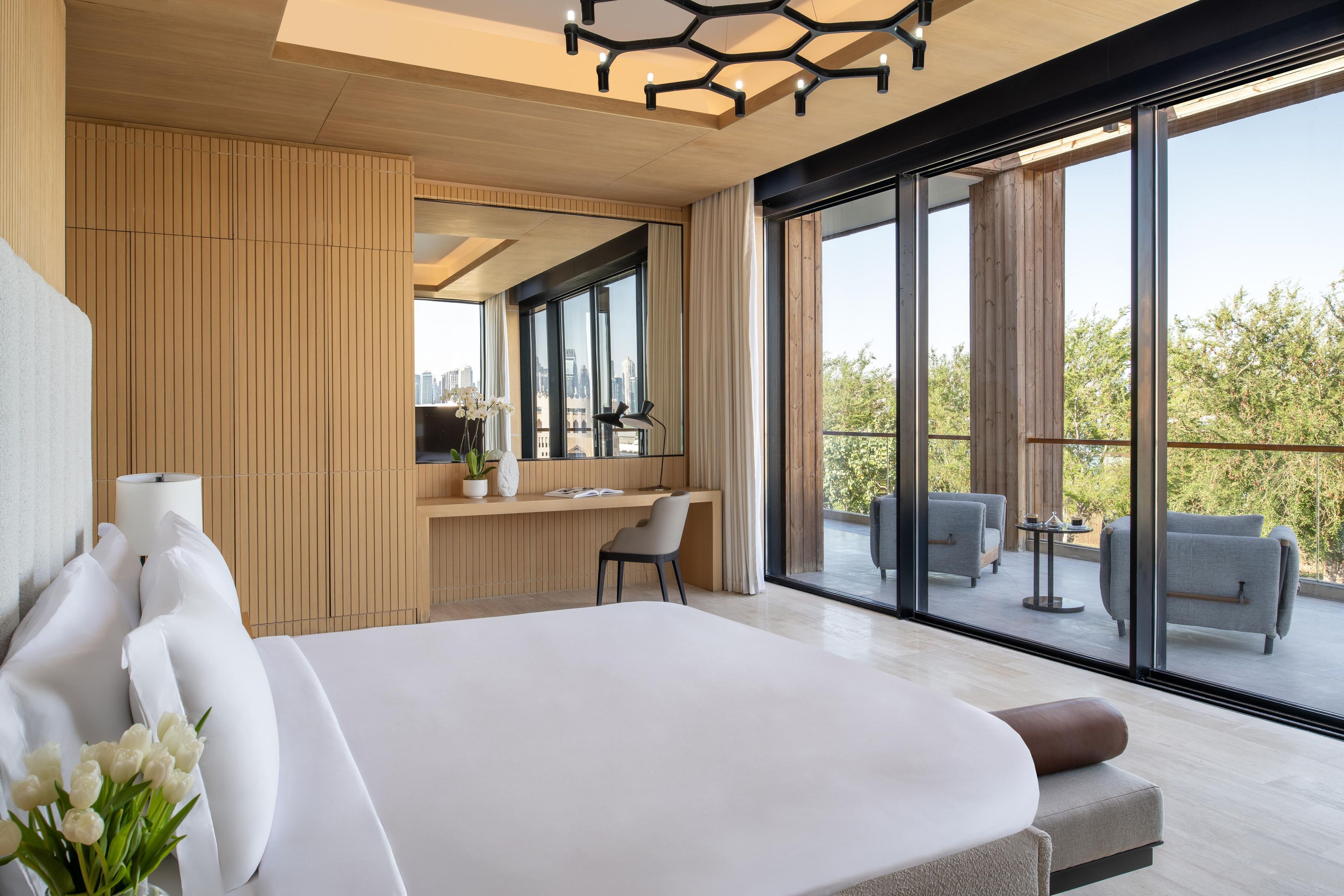 A modern bedroom with a large bed, a desk, and a balcony with seating.