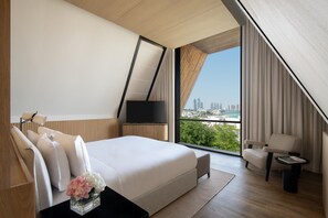 A modern bedroom with a large bed, a TV, and a view of a cityscape. - Katara Hills Doha, Lxr Hotels & Resorts (Doha)