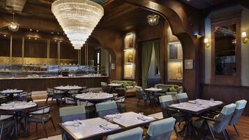 A restaurant with round tables, green upholstered chairs, and a bar area.