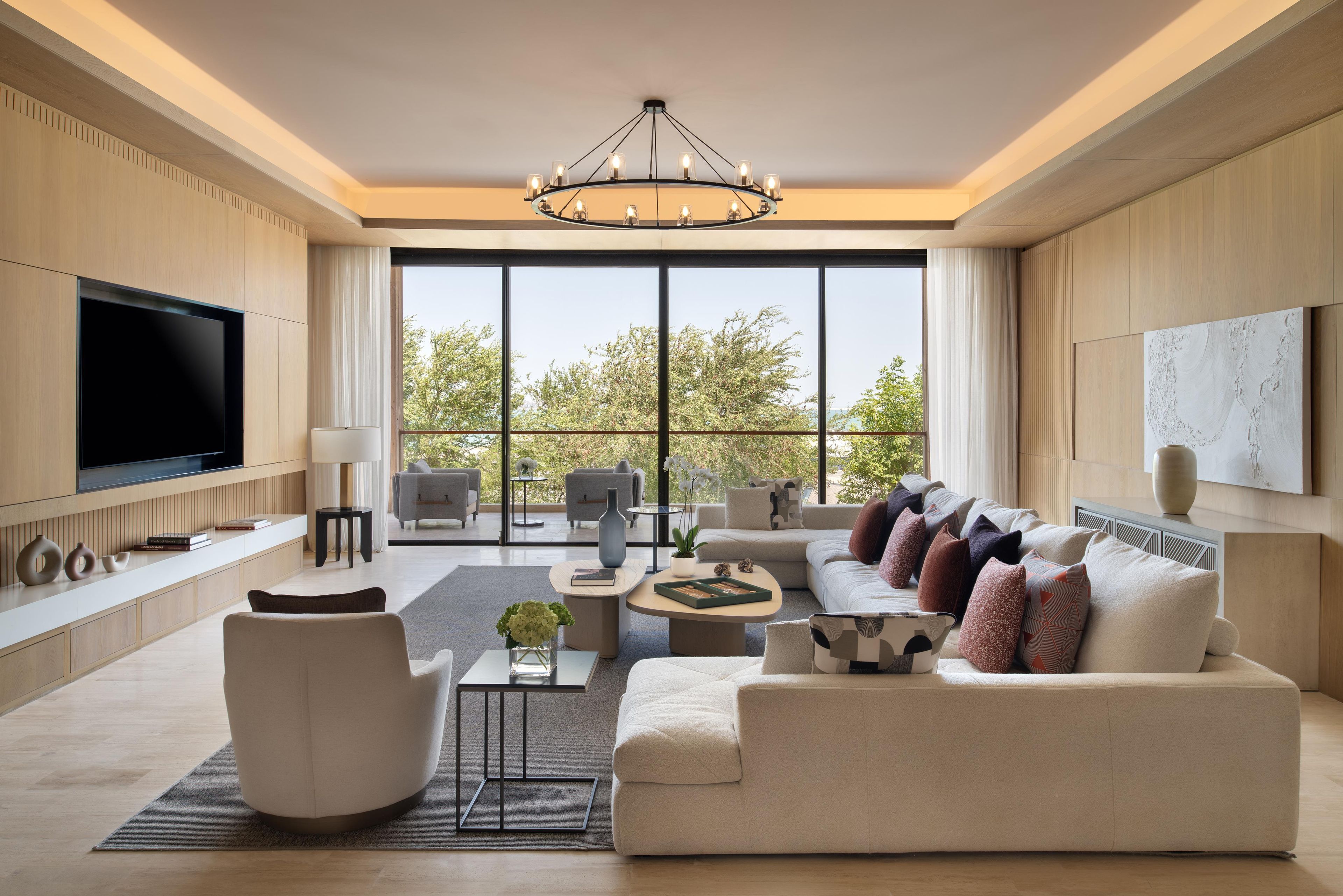 A modern living room with a large TV, comfortable seating, and large windows.