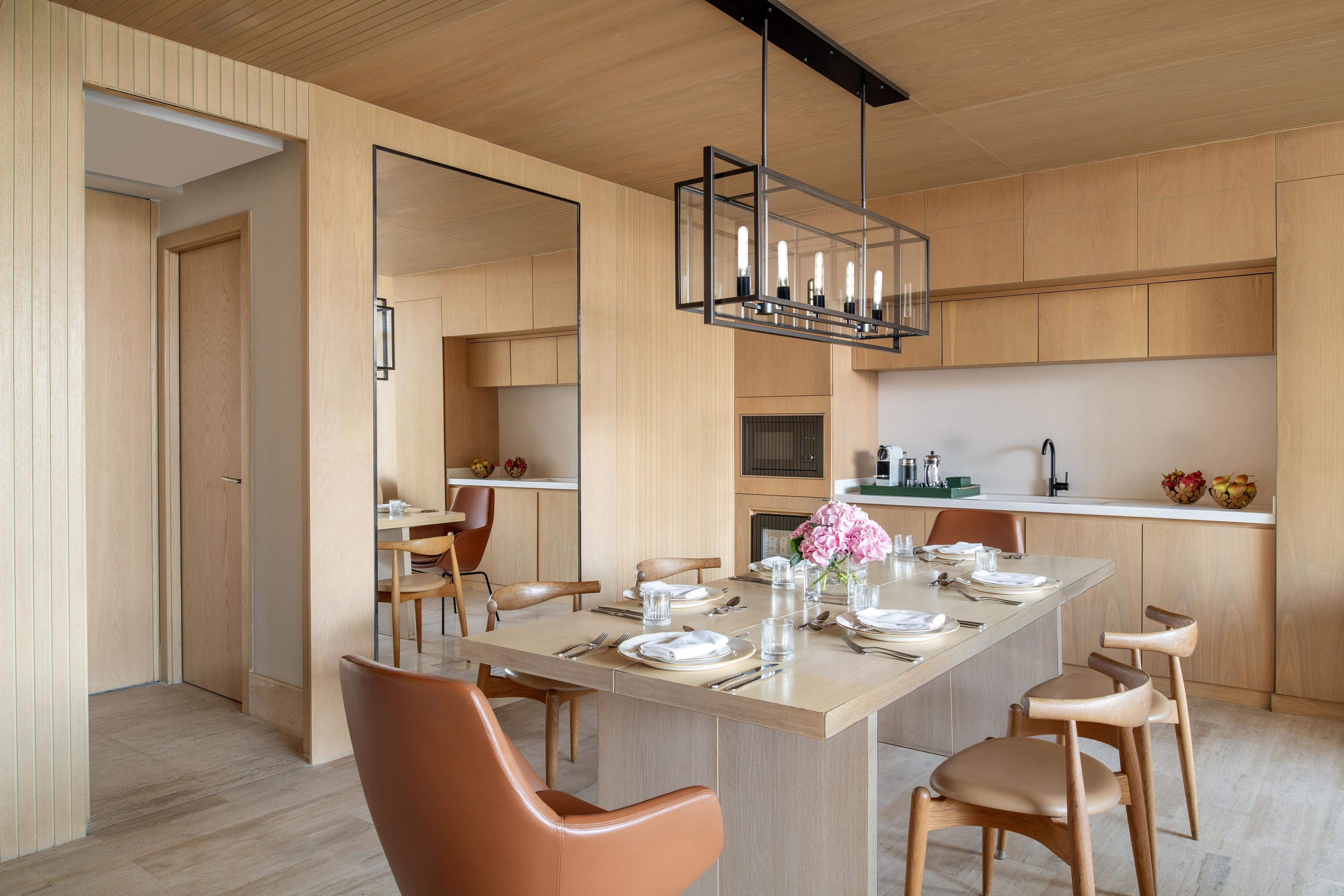 A modern dining area with a wooden table set for four, surrounded by leather chairs.