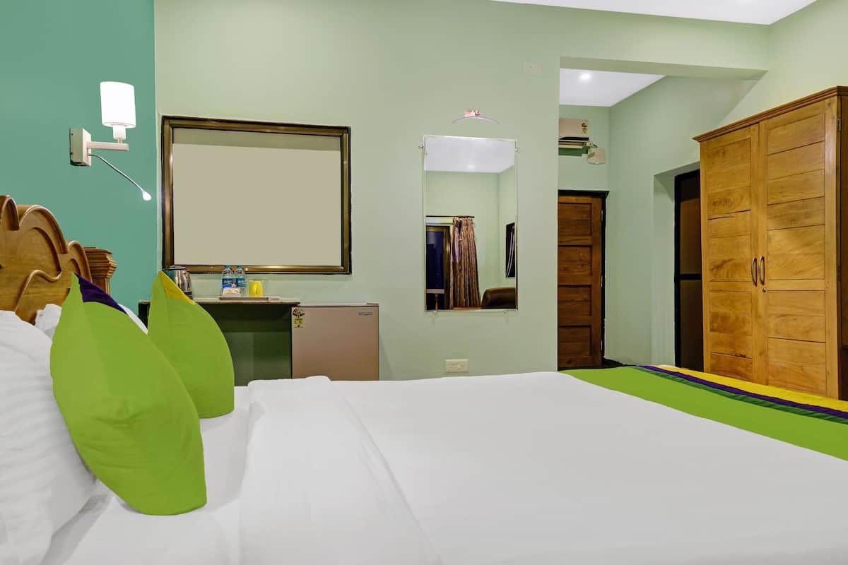 A hotel room with a bed, a desk with a mirror, a wardrobe, and a small refrigerator.