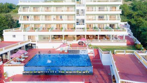 A multi-story hotel with a swimming pool, outdoor seating, and a scenic hillside view. - SPARV Aulakhs Resort (Mandrem)