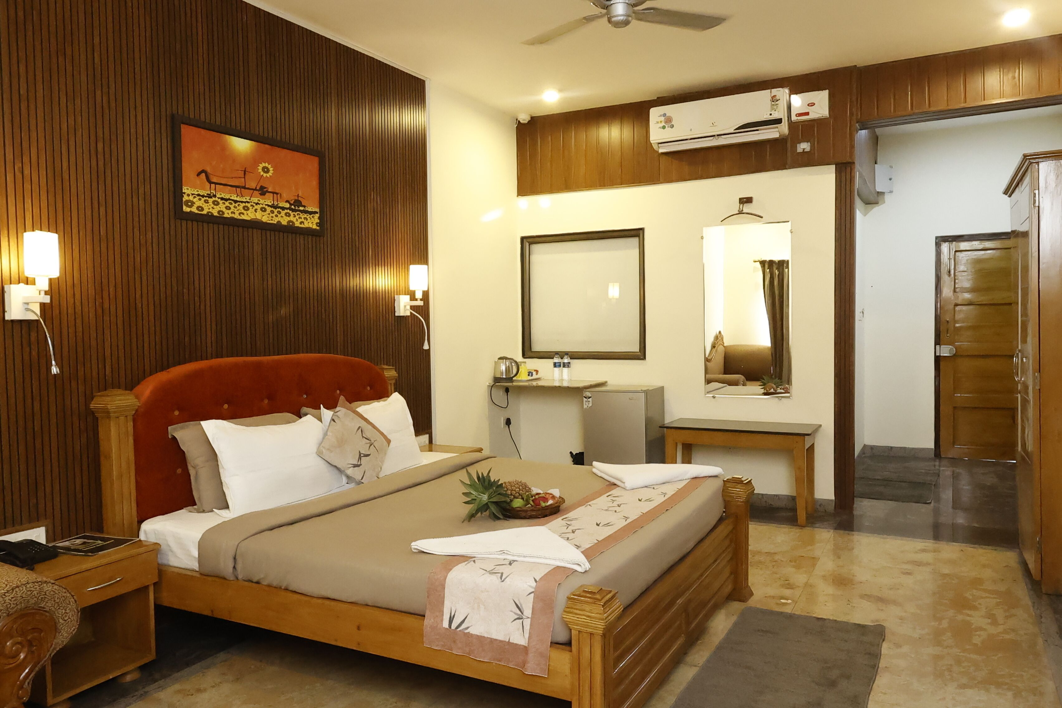 A hotel room with a bed, bedside table, lamp, mirror, and a small desk with a chair.