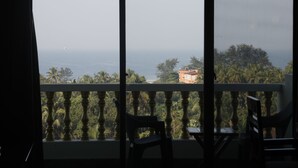 A balcony with a view of the sea, palm trees, and a building in the distance. - SPARV Aulakhs Resort (Mandrem)