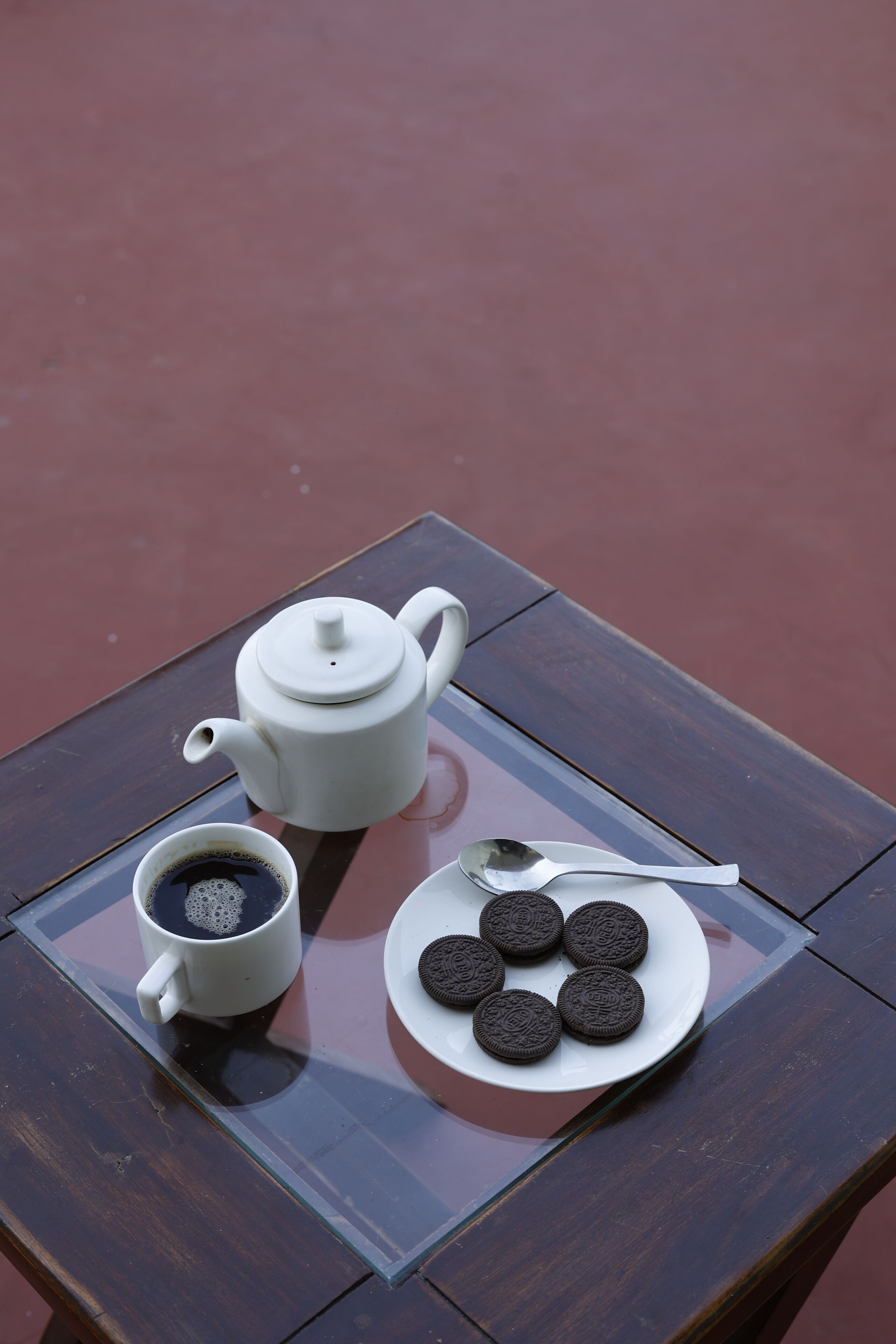 A table with a white teapot, a cup of coffee, and a plate of cookies.