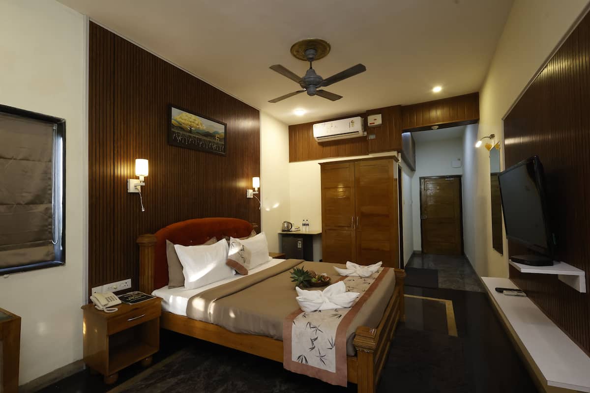 A hotel room with a bed, bedside table, lamp, ceiling fan, wardrobe, TV, and a small desk with a telephone.