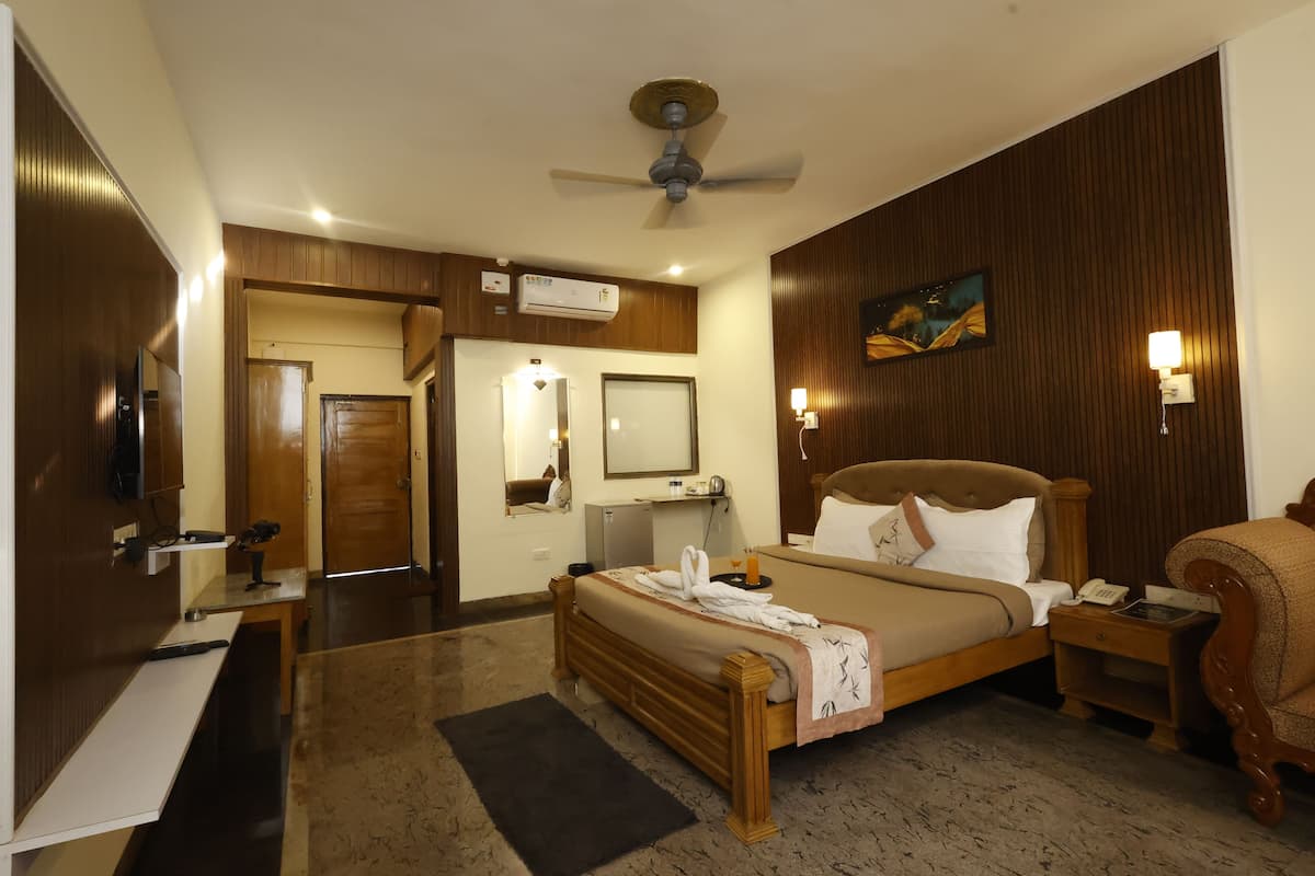 A hotel room with a bed, bedside table, nightstand, ceiling fan, air conditioning unit, and a painting on the wall.