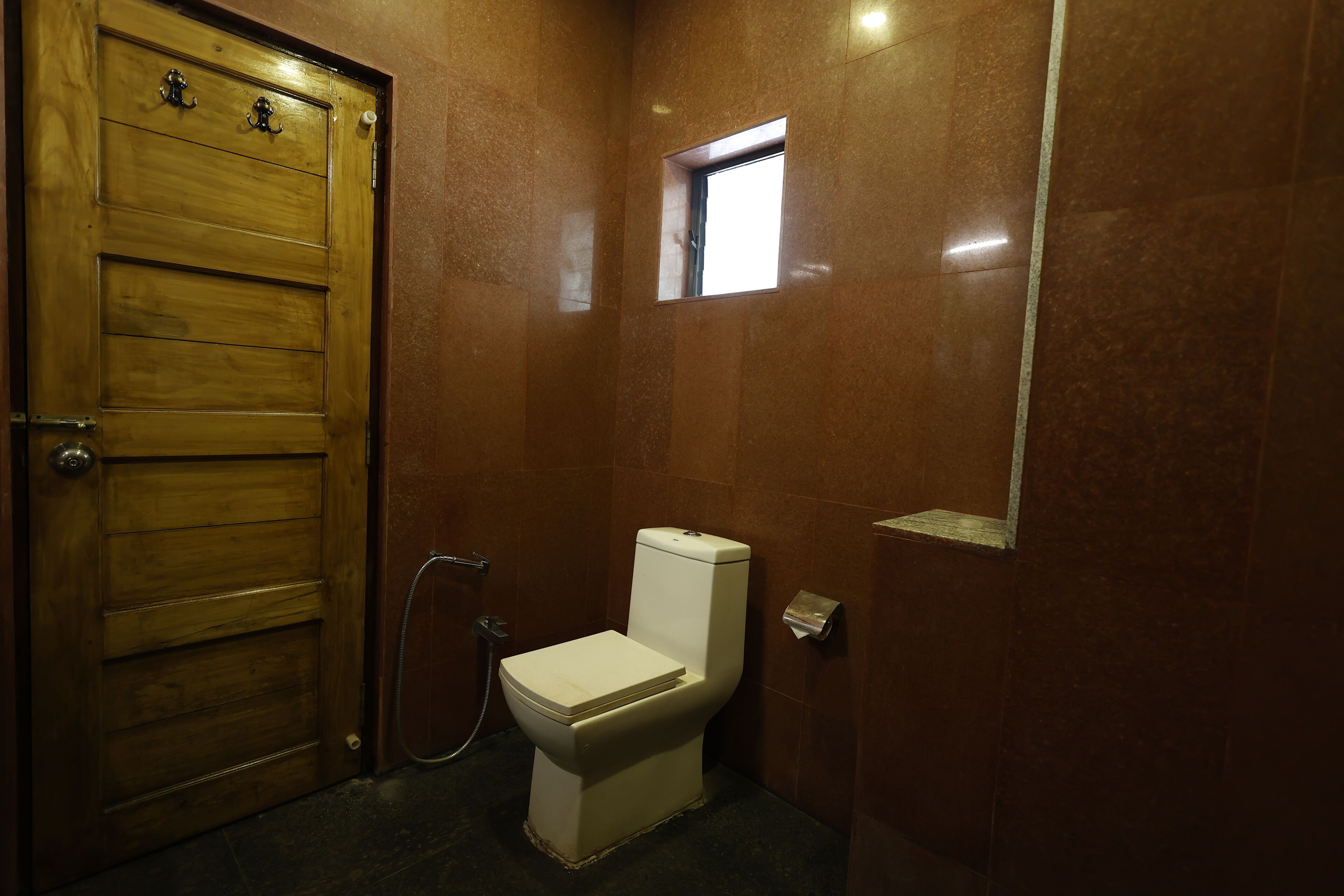 Une salle de bain avec une porte en bois, des toilettes et une petite fenêtre.