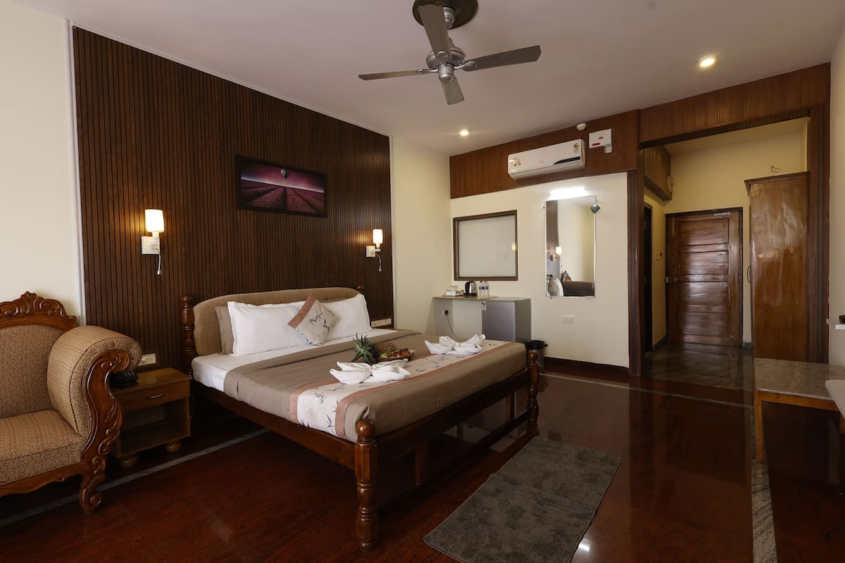 A hotel room with a wooden bed, a nightstand, a chair, a ceiling fan, an air conditioning unit, and a mirror.