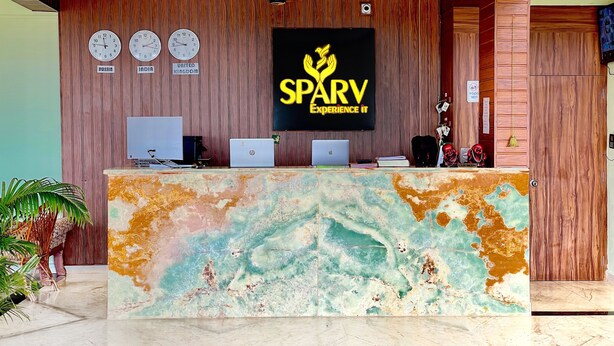 A reception desk with a marble top, wooden paneling on the walls, and clocks displaying different time zones. - SPARV Aulakhs Resort (Mandrem)