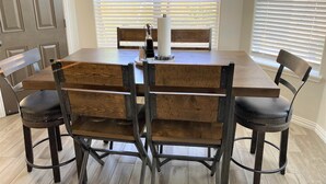 Uma mesa de jantar com tampo de madeira e estrutura de metal, rodeada por quatro cadeiras com estrutura de metal e assentos de madeira.
