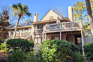 A two-story house with a balcony, surrounded by greenery and trees.