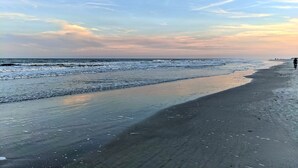 Uma praia com extensa faixa de areia e ondas suaves.