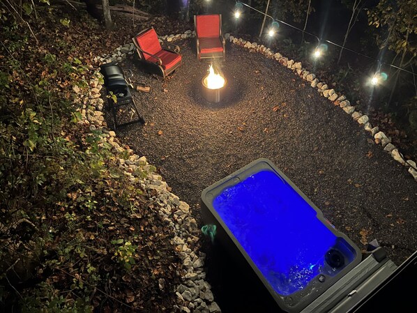 A hot tub surrounded by a stone border, with two red chairs and a fire pit in the center. - Romantic Red River Gorge Cabin • Hot Tub • Quiet Escape (Stanton)