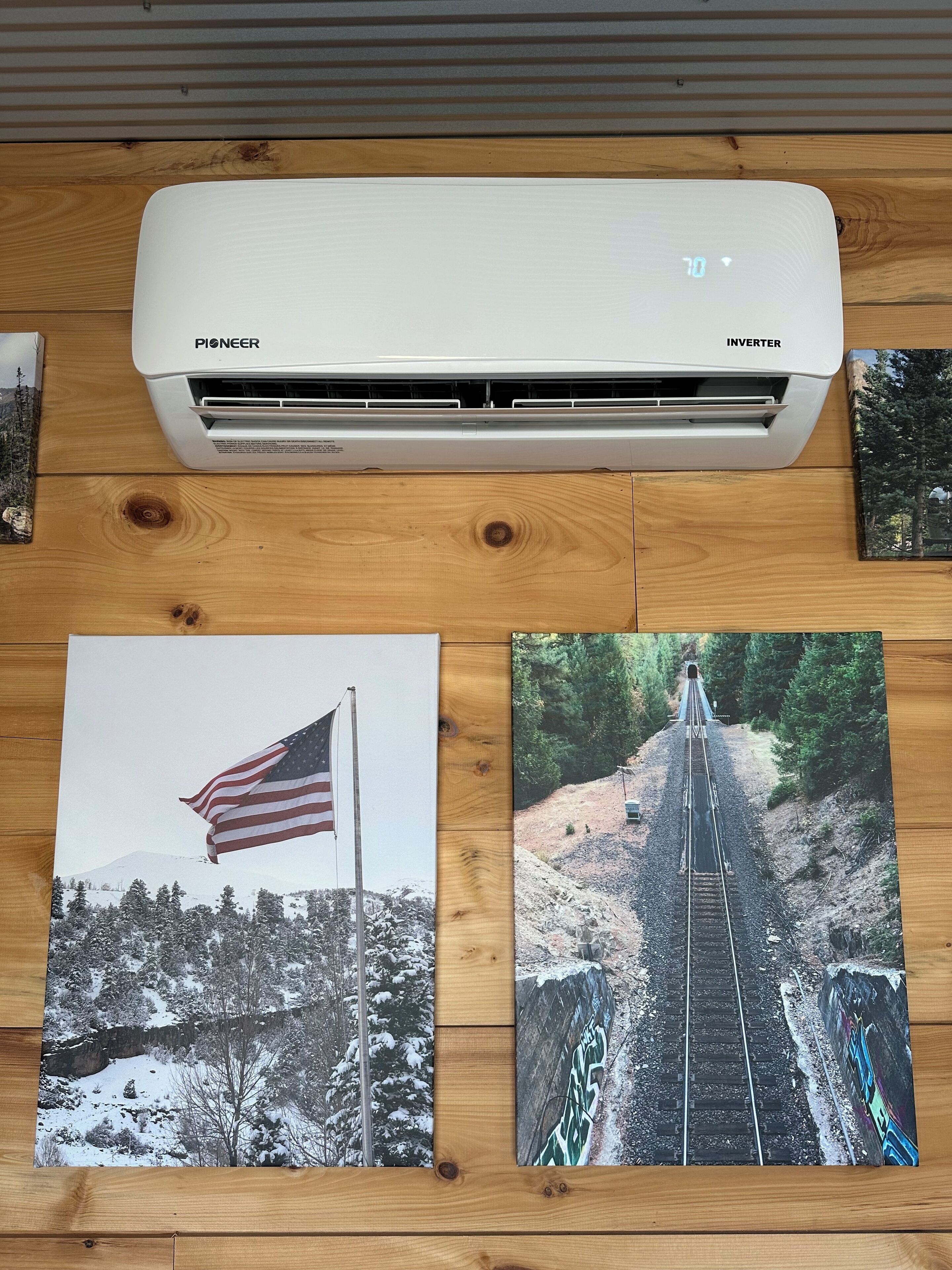 A Pioneer Inverter air conditioner on a wooden surface with three photographs of landscapes.