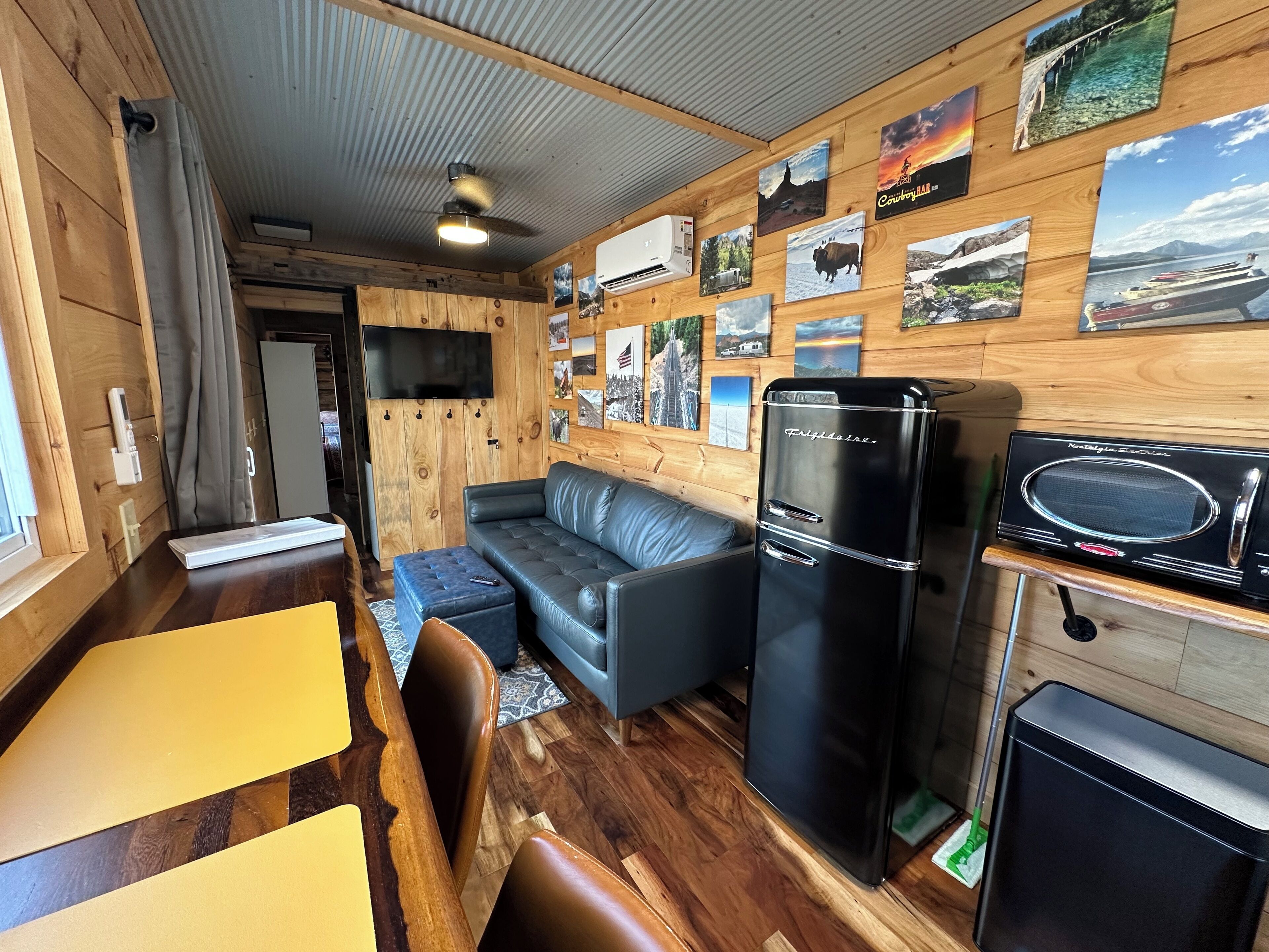 Una cabaña compacta y moderna con interior de madera, un sofá, una mesa de comedor, un refrigerador y un microondas.