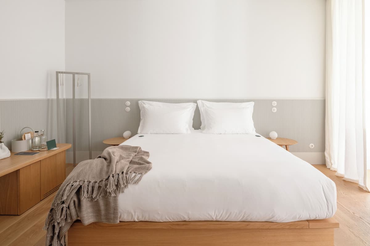 A minimalist bedroom with a large bed, wooden nightstands, and a bedside table with a lamp.