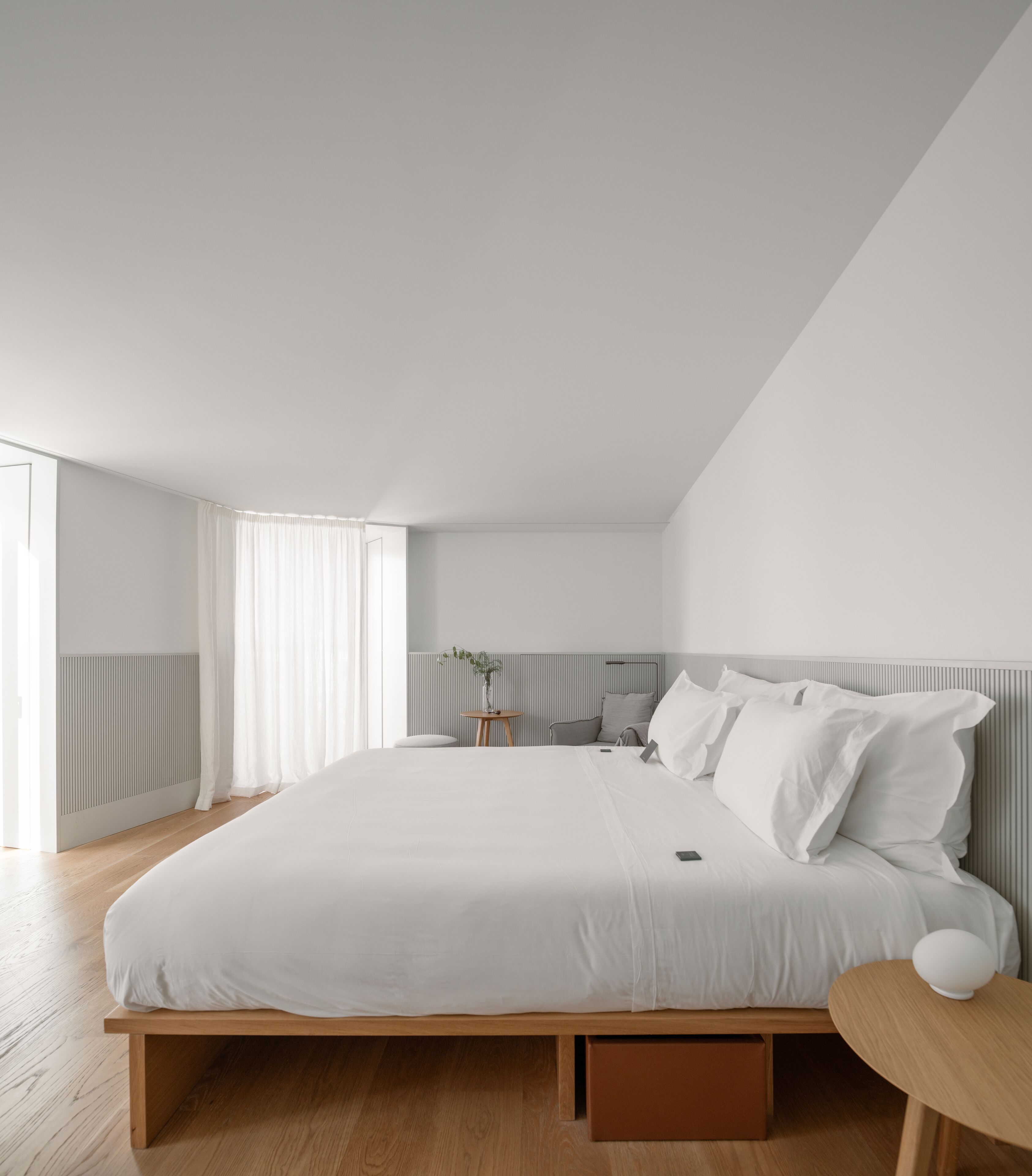 Une chambre à coucher moderne avec un grand lit, une table de chevet, une petite table ronde et une commode.