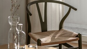 Una mesa de madera con una silla tejida, un florero de vidrio y una vela.