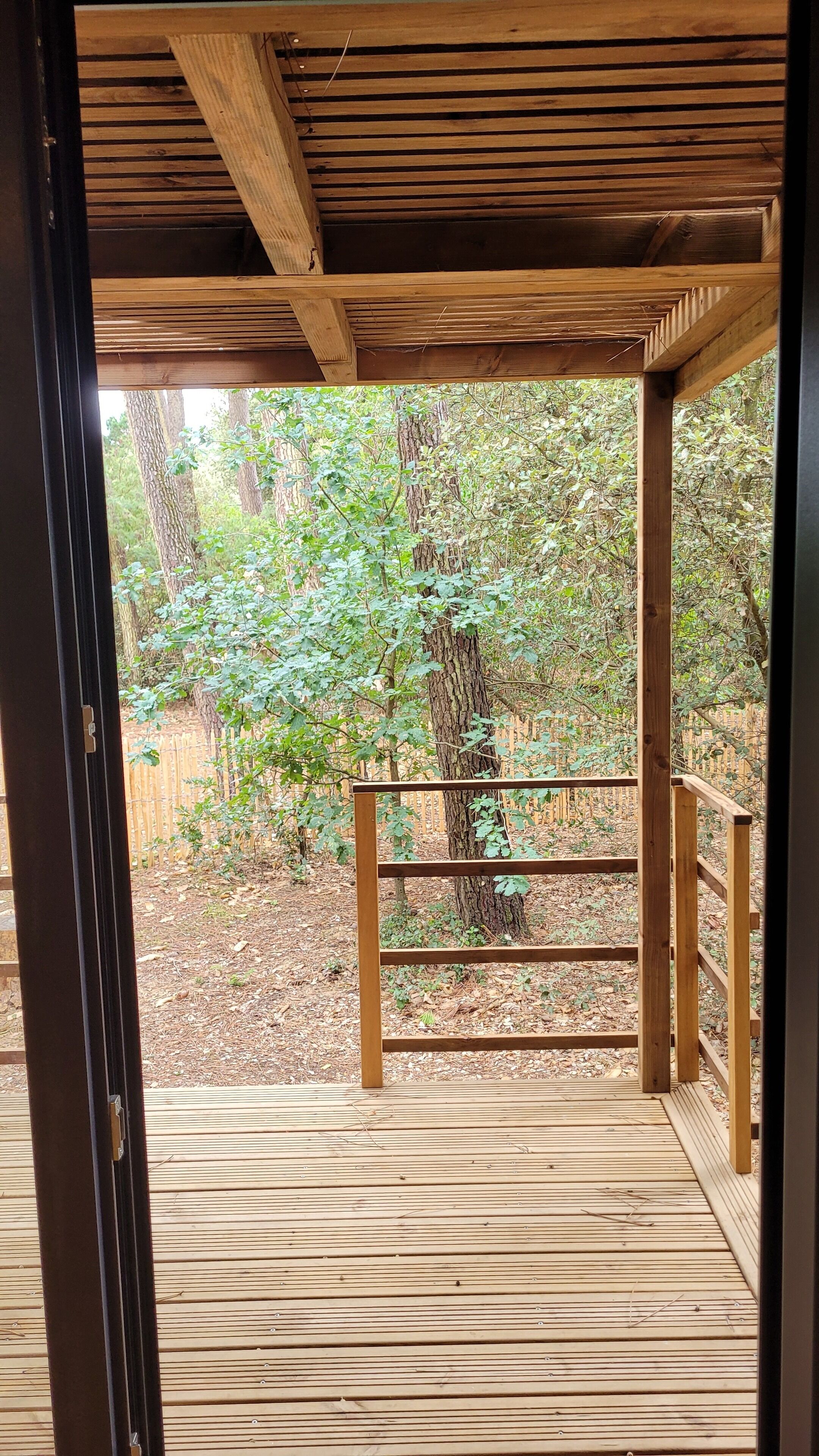 A wooden deck with a railing, surrounded by trees and a wooden fence.