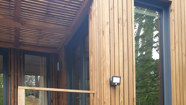 Una cabaña de madera con un porche cubierto, un pequeño espacio de descanso con sillas y un ventanal grande.