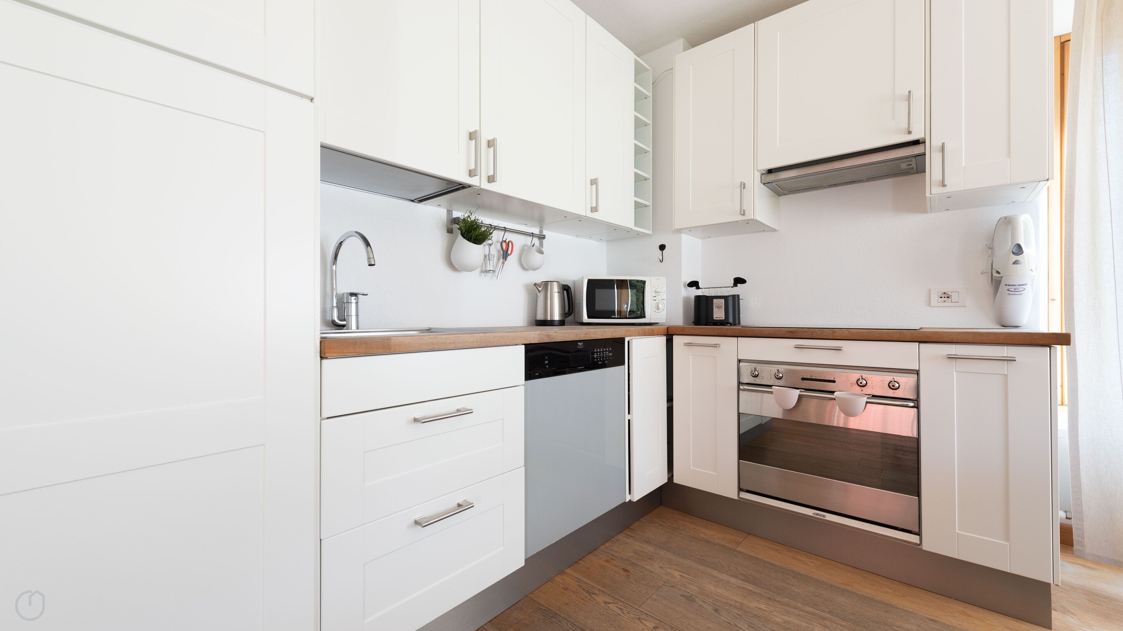 A modern kitchen with white cabinets, stainless steel appliances, and a wooden countertop.