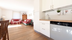 A modern kitchen with white cabinets, a dishwasher, and a sink. There is a dining area with a wooden table and chairs. - Milano 35 (Bormio)
