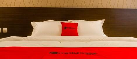 Une chambre d’hôtel avec un lit parfaitement fait, un oreiller rouge orné du logo RedDoor et une couvre-lit rouge portant le même logo.