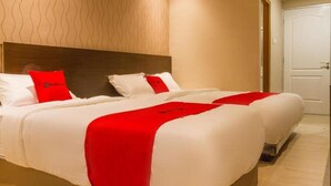 A hotel room with two beds, each with white bedding and red accents, a wooden headboard, and a plain wall with a wavy pattern. - Reddoorz Plus @ Dipatiukur (Bandung)
