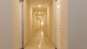 A long, well-lit hallway with doors on both sides, leading to multiple rooms. - Reddoorz Plus @ Dipatiukur (Bandung)