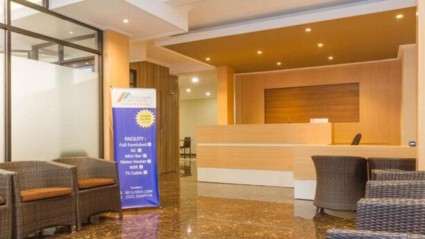 A reception area with a wooden reception desk, wicker chairs, and a banner advertising guest house features. - Reddoorz Plus @ Dipatiukur (Bandung)