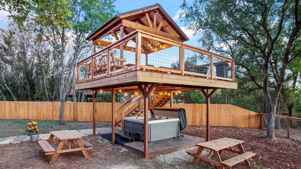 A wooden deck structure with a hot tub and picnic tables. - Guadalupe Bluff Bunk House 5 Bedroom Home by RedAwning (Kerrville)