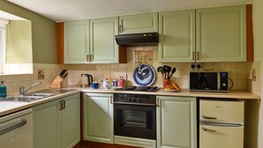 A kitchen with green cabinets, a stove, oven, microwave, and a refrigerator. - The Cottage at Greystoke (Greystoke)